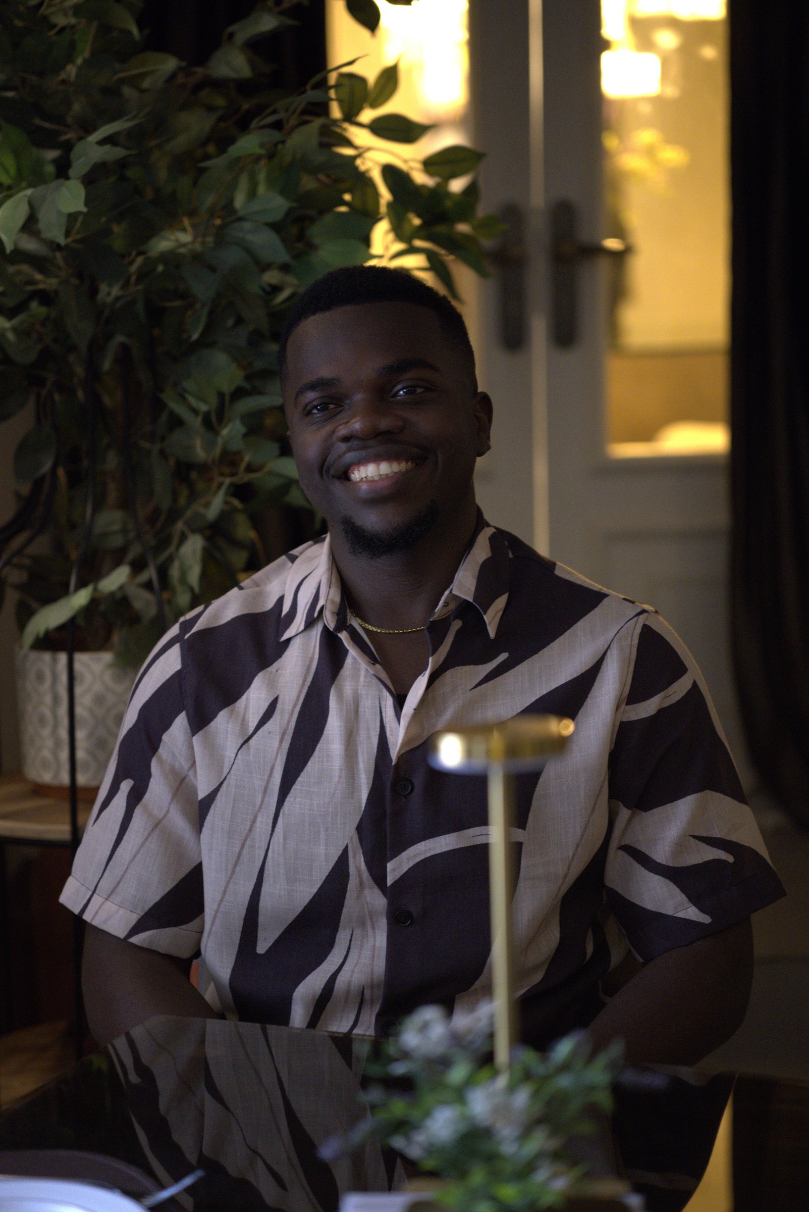 Nnaemeka Nnam in a patterned shirt, smiling in warm dim evening light